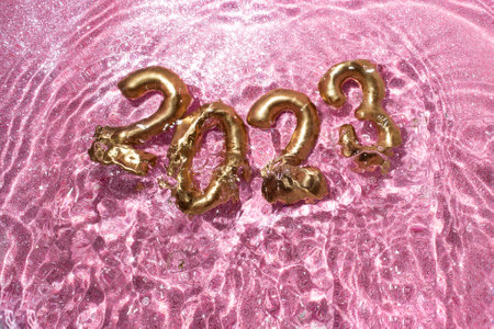2023 golden number splashing in pink glittery water. Happy new year creative concept.