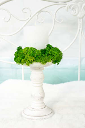 Wood candle holder with a white candle surrounded by moss, on white and light blue festive background. Wedding setting backdrop.の写真素材
