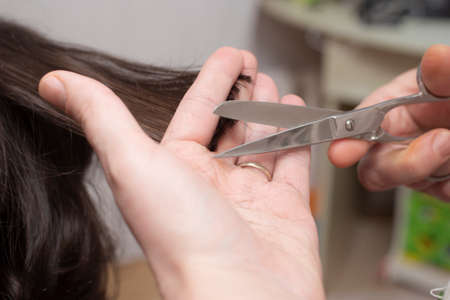 Mother's hands with scissors, trimming her son's hair at home. Soft focus close up.の写真素材