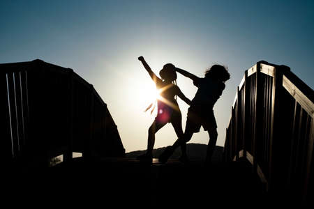 Boy and girl silhouettes dancing on a bridge against the sunset sunの写真素材