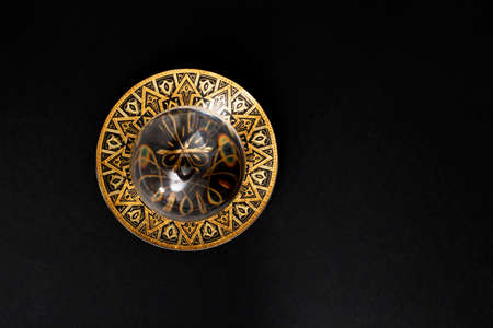 Defocused lens ball on a golden metal tray, isolated on black background. Flat lay close up.