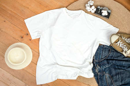 Unisex white shirt , flat lay on wooden boards with blue jeans, sneakers and cotton flowers,...