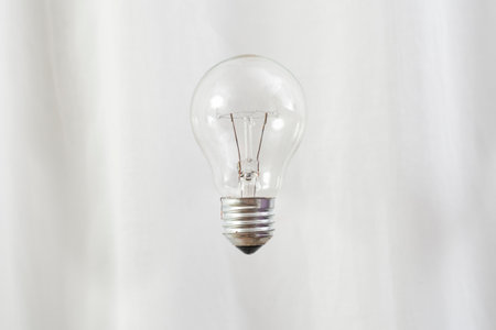 Transparent lightbulb levitating on white drapes background.