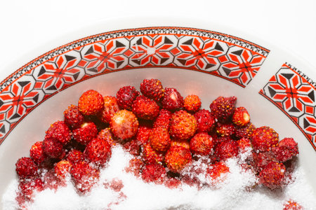 Wild strawberries (Fragaria vesca) with sugar crystals, on a bowl with romanian ethnic motifs.