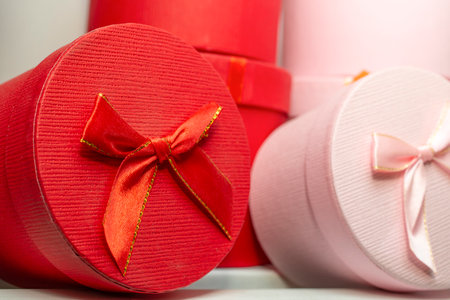 two cylindrical present boxes , red and pink, with satin ribbons side view close up