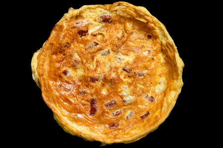 prepared round omelette with sausages, isolated on black background, with intentionally underexposed...