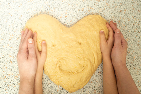 Mother and son hands holding dough in the shape of a heart with a smiley face, soft focus close upの写真素材
