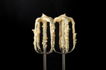 Mixer whisks with yellow mayonnaise, isolated on black background, soft focus close upの写真素材