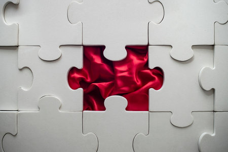 white jigsaw puzzle with a missing piece, and red satin foldsの写真素材