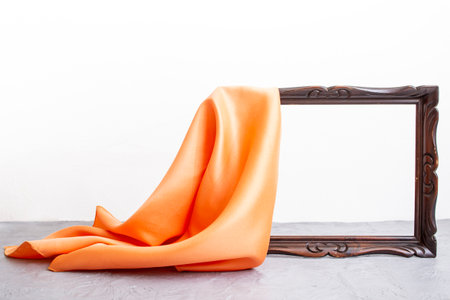 Orange satin cloth unveiling a wooden brown frame, on cement table top and white background, mockup for presentationの写真素材