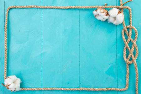 Jute rope rectangular frame, with a knot and cotton flowers, on blue painted boards, navy backdropの写真素材