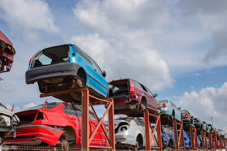 Stacked cars on a metallic frame, used for parts. Scrapyard perspective with blue skies and fluffy...