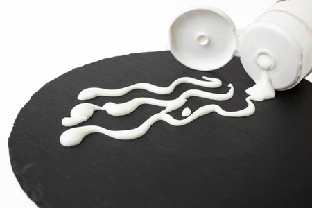 White cream waves on black stone texture, from a plastic cap tube, soft focus close up