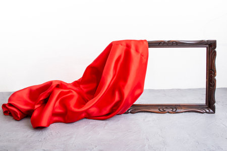 Red satin cloth unveiling a wooden brown frame, on cement table top and white background, mockup for presentationの写真素材