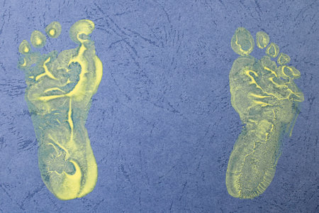 Baby feet prints made with yellow paint on blue textured paper, creating memories conceptの写真素材