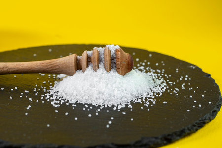 honey dripper in a pile of sugar crystals, on a black stone tile, close upの写真素材