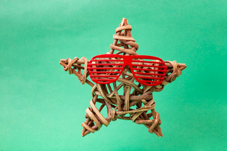 star made of bended wood twigs, and a pair of retro striped red glasses, levitating on green backgroundの写真素材