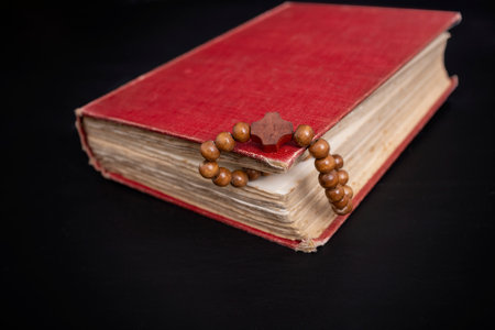 Wooden beads on a string between the pages of a red hard cover book, on dark background. prayer conceptの写真素材