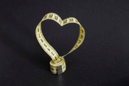 Rolled yellow tape measure in the shape of a heart, isolated on black background.の写真素材