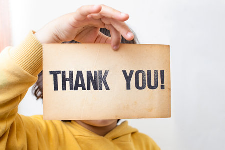 Caucasian male child holding a piece of vintage yellowed paper with Thank you! written with stamp letters.の写真素材