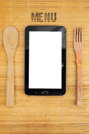 Empty display of a tablet, with wooden spoon and fork, on bamboo placemat backgroundの写真素材
