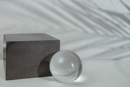Empty gray backdrop with a cube and a glass sphere on a gray background with palm leaves shadows, soft focusの写真素材