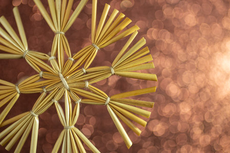 Christmas snowflake decoration made with golden straws and thread on brown defocused glitter background, soft focusの写真素材