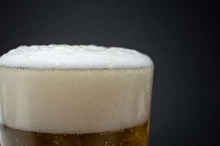 Transparent glass filled with golden beer and foam, side view close up crop, soft focusの写真素材