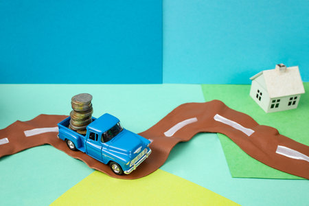 Die cast toy car transporting a stack of coins to a miniature houseの写真素材