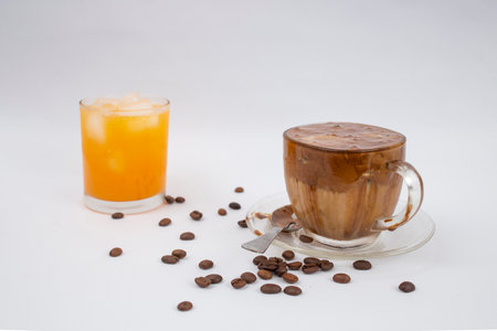 Home made dalgona coffee with scattered coffee beans and a glass of fresh orange juice