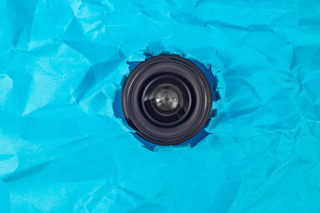 Camera lens taking pictures thru a torn hole in blue crumpled paper, soft focus