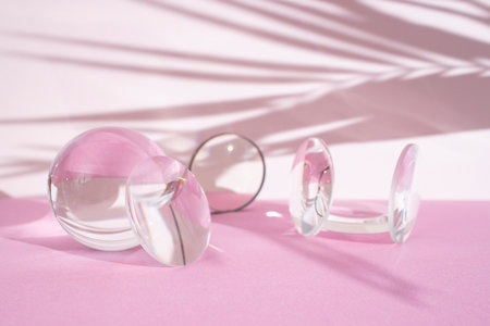 Clear magnifying lenses on bright pink and beige background, with palm leaves shadowsの写真素材