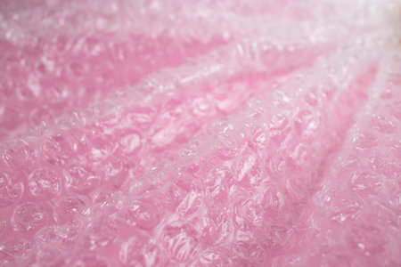 Plastic bubble wrap foil creases and waves on pink background, abstract textured backdrop, soft...