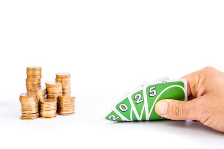 Hand holding green cards with 2025 numbers, and  defocused stacks of golden coins in the background, isolated on white background, gambling   conceptの写真素材