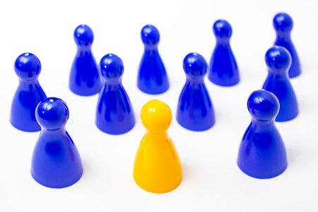 One yellow pawn in a crowd of many blue pawns isolated on white background, soft focusの写真素材