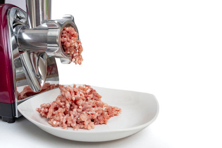 Electric grinder with minced pork meat and a white plate on whiteの写真素材