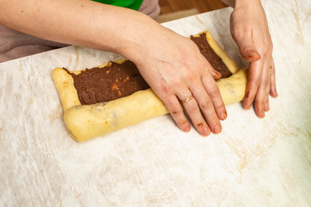 Hands rolling raw dough with cocoa, walnuts and sweet filling for cozonac