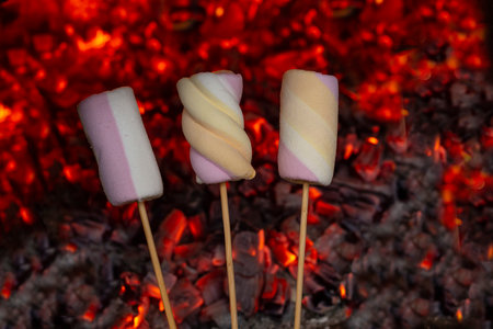 Three marshmallows on wooden skewers over red burning coal background, soft focusの写真素材