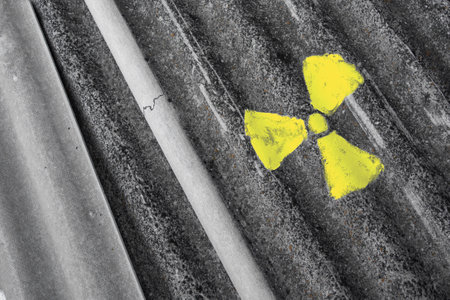Radioactive symbol smudged with yellow paint on weathered wavy asbestos sheet, abstract close upの写真素材