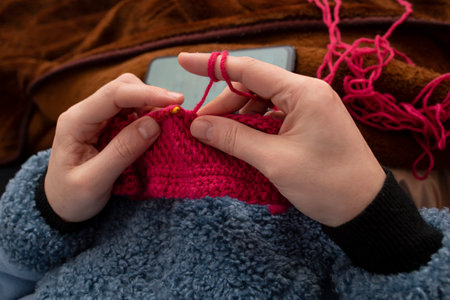 Woman hands knitting with a crochet hook and red thread , learning with a smartphone tutorial, soft focusの写真素材