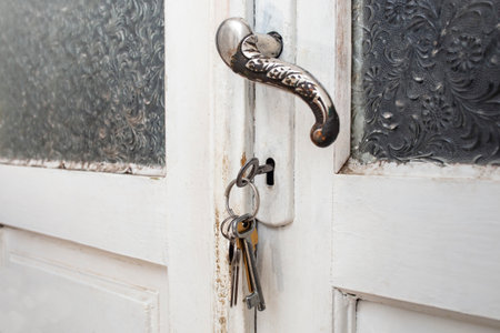 Vintage white door with white peeling paint, corrugated glass windows and old fashioned key bunch, soft focusの写真素材