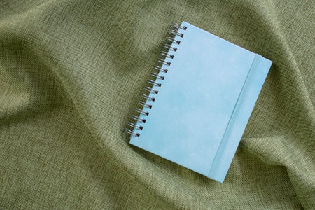 Empty blue hard cover notebook   on olive green fabric backdrop, copy space for text