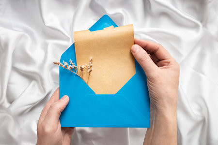 Woman hands opening and pulling an empty yellowed paper scroll from a blue envelope on white silky background, soft focus close up, greeting cardの写真素材