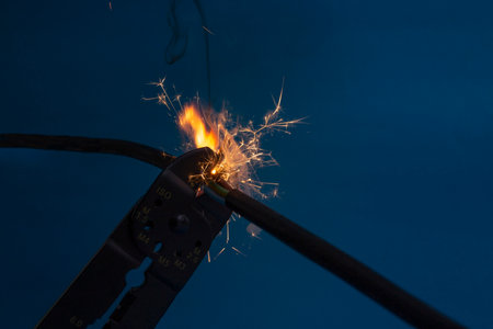 flame and sparks with wire stripper cutting  electrical cables, on dark blue color background , at night , fire hazard concept, soft focusの写真素材