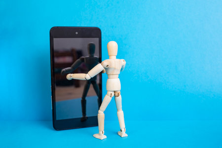 Wooden mannequin embracing a smartphone on blue background, taking a selfie conceptの写真素材