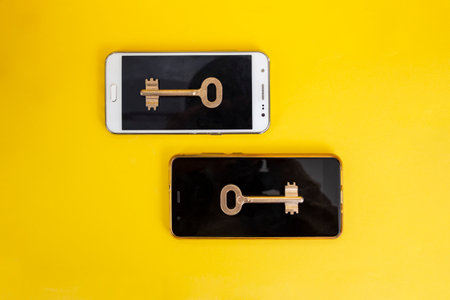 Two vintage golden keys on smartphones on yellow background