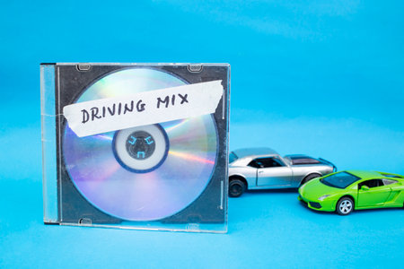 Compact disk next to toy cars on blue background and driving mix words hand written on tapeの写真素材