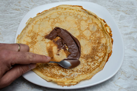 Spreading chocolate cream on a crepe pancake with a silver  spoonの写真素材