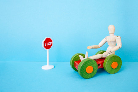 Wooden mannequin on a colored wood stripped toy car next to a red stop sign on blue background,