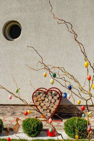 Colorful easter eggs hanging on tree branches in front of a gray house
